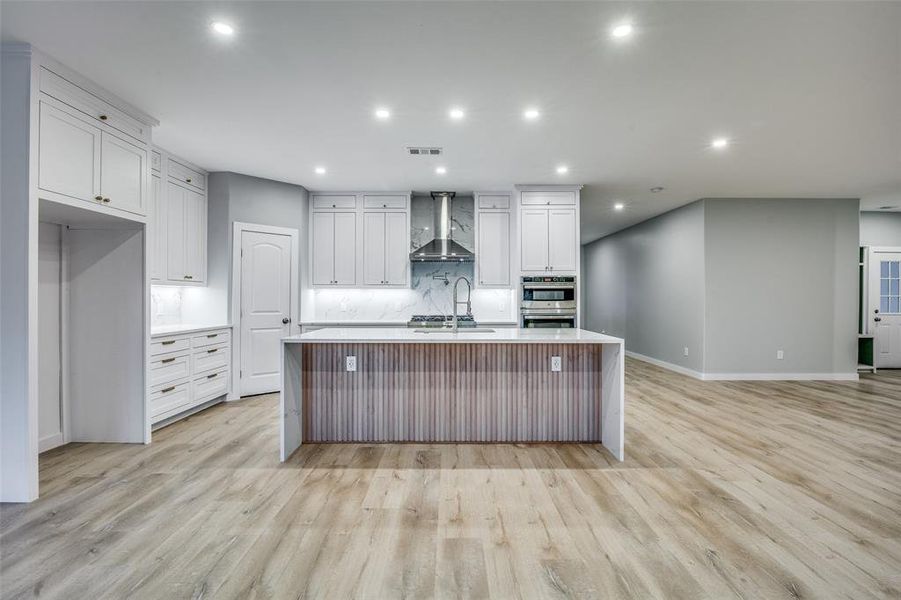 Kitchen featuring white cabinets, a center island with sink, light hardwood / wood-style flooring, and wall chimney range hood