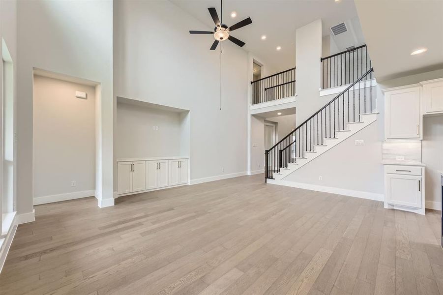 Unfurnished living room with a high ceiling, a ceiling fan, light wood-style floors, stairway, and baseboards
