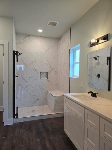 Bathroom featuring vanity, a marble finish shower, and dark wood-style flooring
