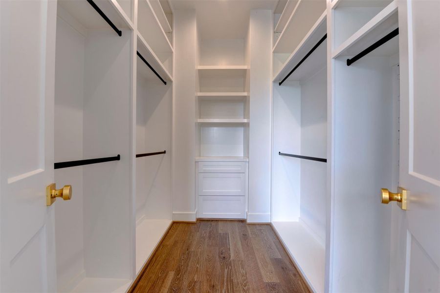 Spacious walk-in closet with ample shelving and hanging space, featuring polished wood floors and bright white cabinetry for a clean, modern look.