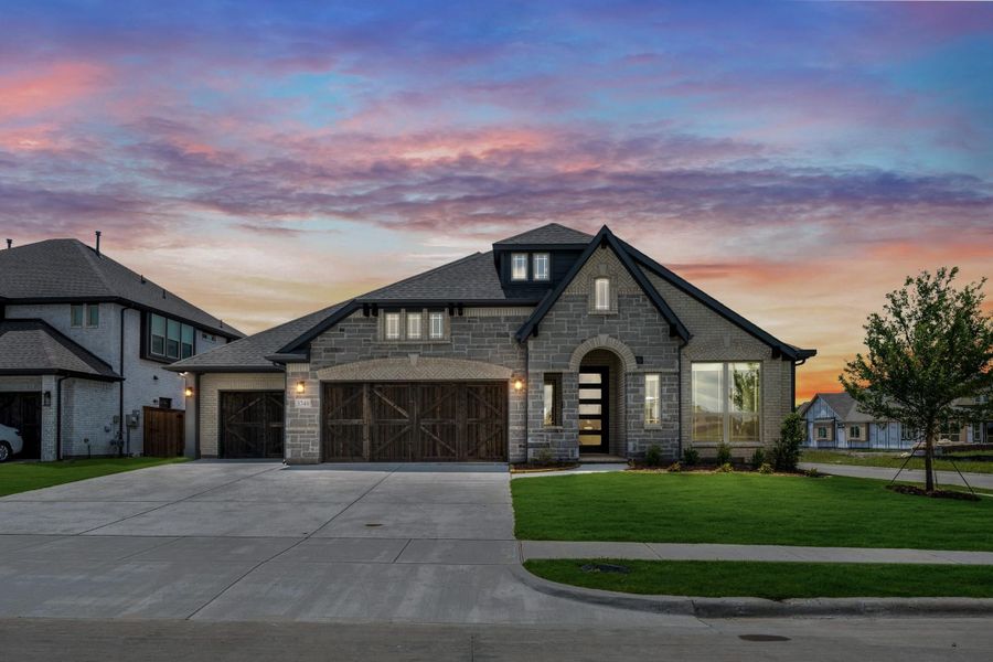 Single-story stone home with two-car garage, arched entry, and large front windows at sunset