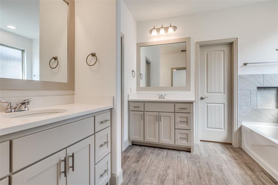 Full bath with a garden tub, two vanities, and light wood-style flooring Full bath with a garden tub, two vanities, and light wood-style flooring