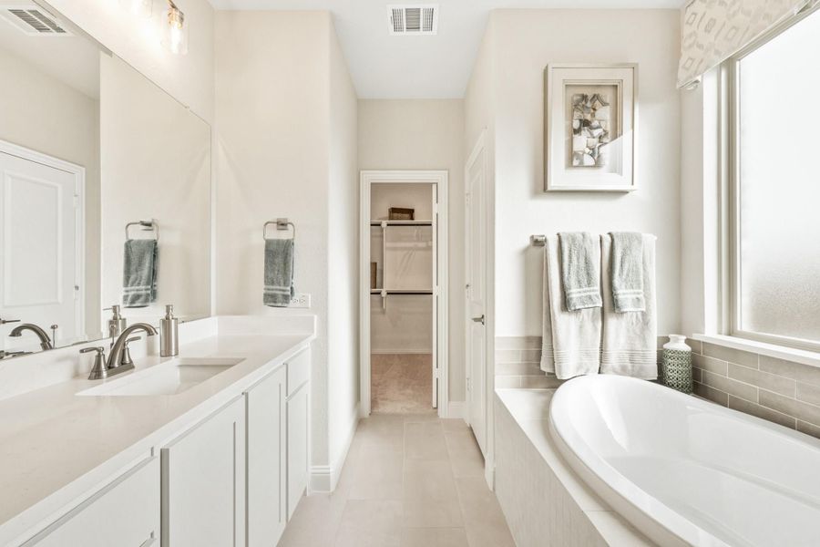 Master bathroom with white double vanity, soaking tub, and walk-in closet access Master bathroom with white double vanity, soaking tub, and walk-in closet access