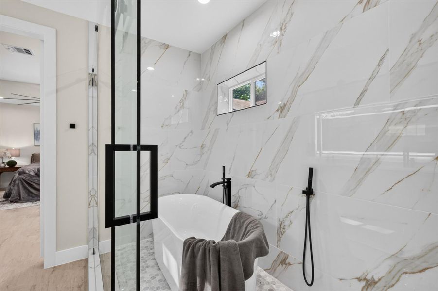 Luxurious bathroom featuring a sleek freestanding tub, elegant marble-patterned tiles, and modern black fixtures, creating a spa-like retreat.