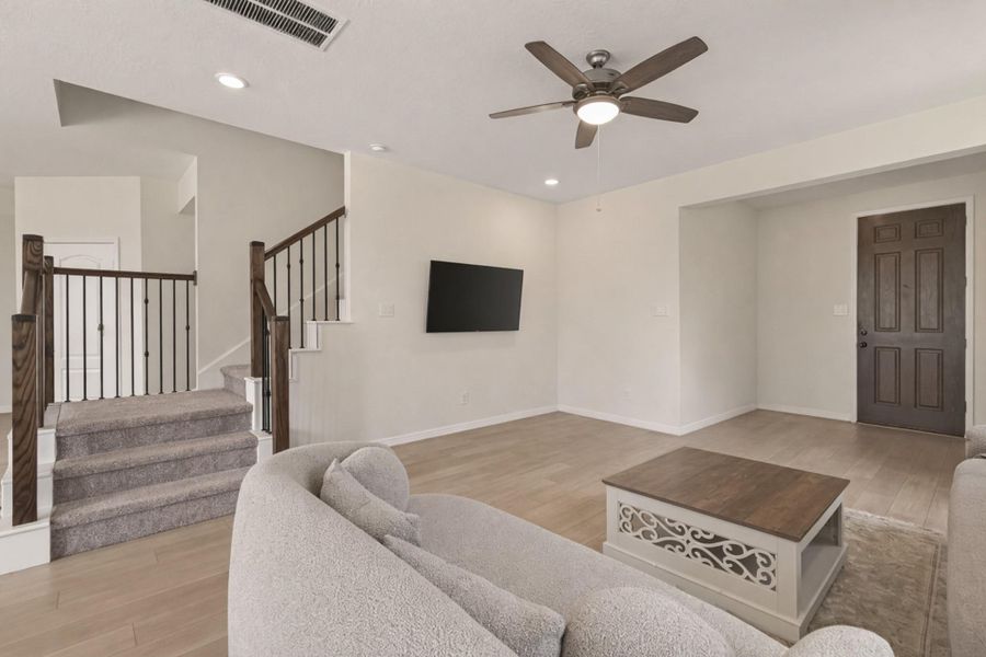 Bright open living room with upgraded light wood floors, recessed lighting, and an elegant staircase.