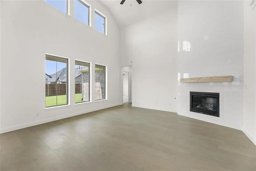 Unfurnished living room featuring ceiling fan, a large fireplace, a towering ceiling, and dark hardwood / wood-style floors