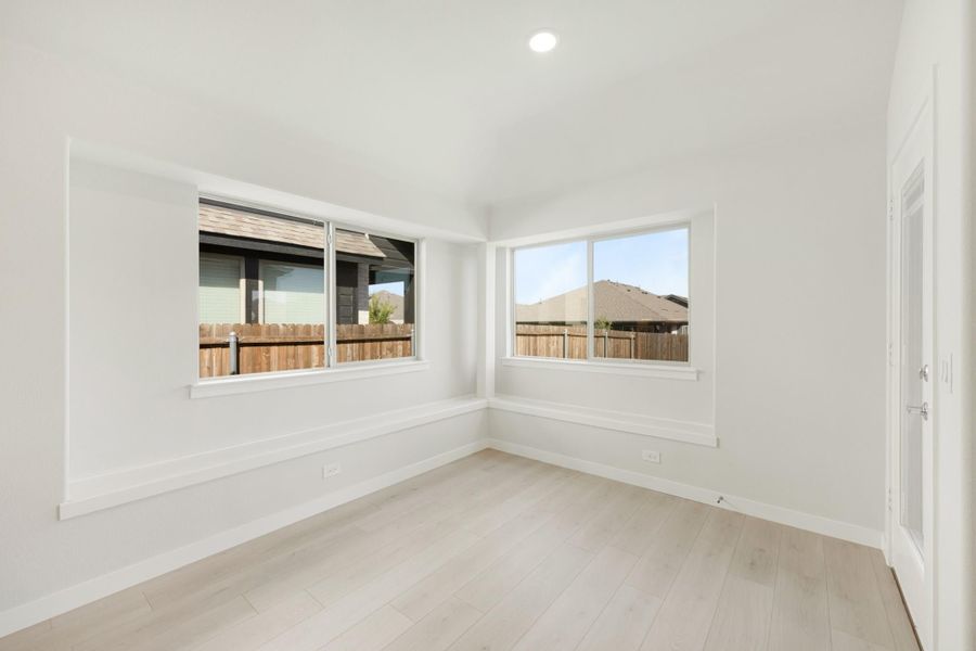 Empty bedroom with light hardwood floors, white walls, and two corner windows with backyard views.