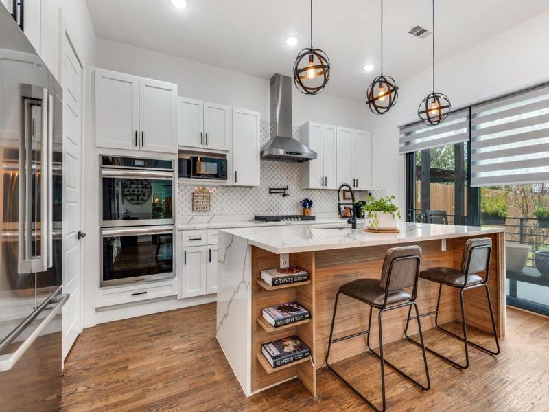 Kitchen featuring appliances with stainless steel finishes, pendant lighting, light stone counters, white cabinets, and a breakfast bar