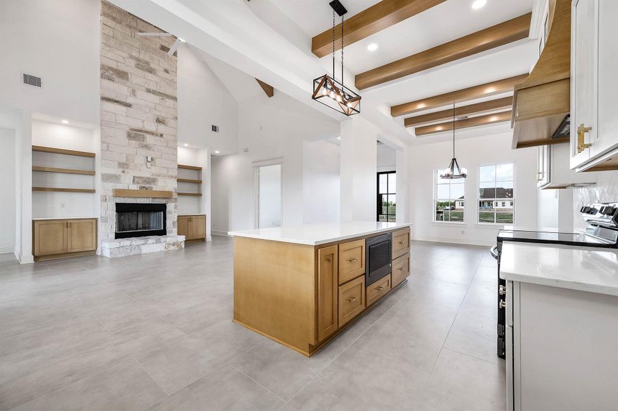 A wide view of the open living and kitchen area, featuring a floor-to-ceiling fireplace, built-in shelving, exposed wood beams, and a spacious center island.