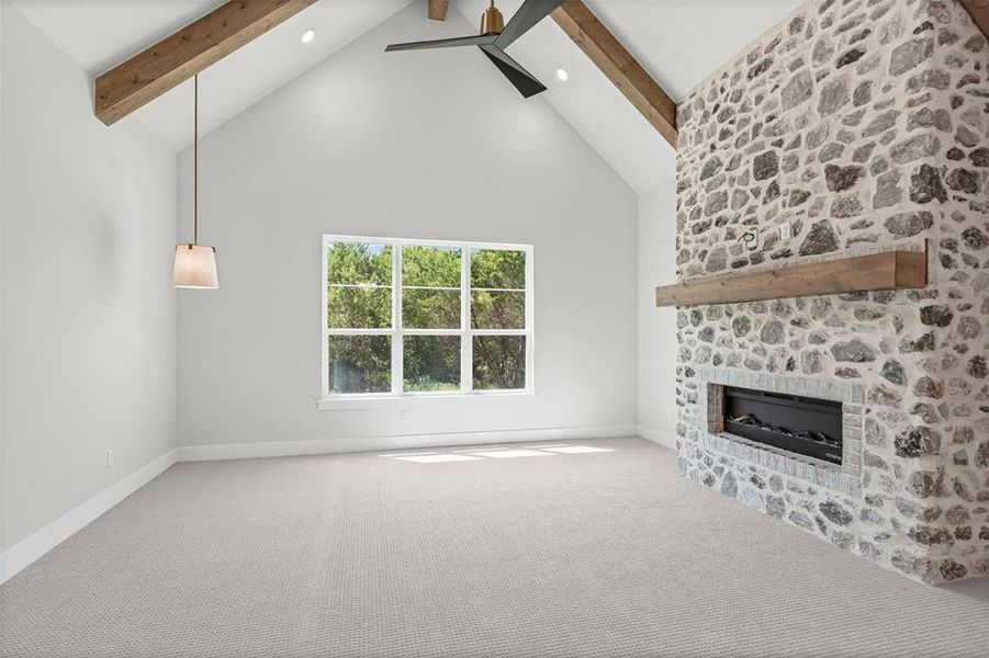 Unfurnished living room featuring beam ceiling, high vaulted ceiling, carpet, a stone fireplace, and ceiling fan Unfurnished living room featuring beam ceiling, high vaulted ceiling, carpet, a stone fireplace, and ceiling fan