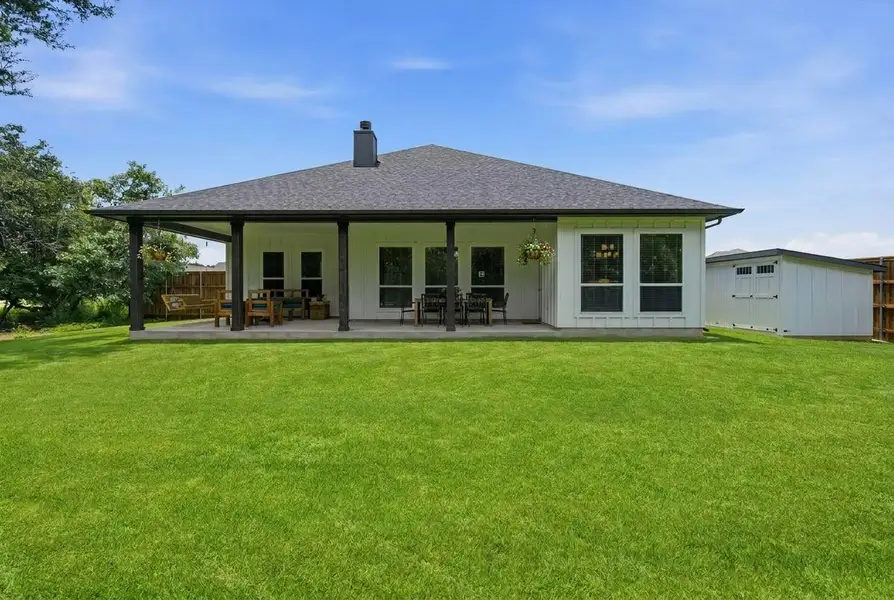 A deep green lawn stretches before a residence featuring an inviting covered patio and a practical storage shed. A deep green lawn stretches before a residence featuring an inviting covered patio and a practical storage shed.