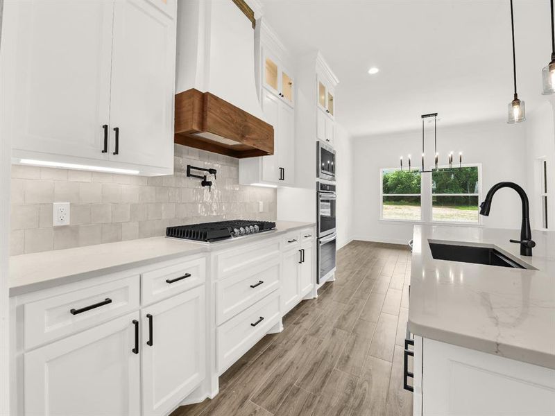 Kitchen with a sink, appliances with stainless steel finishes, custom range hood, backsplash, and white cabinetry Kitchen with a sink, appliances with stainless steel finishes, custom range hood, backsplash, and white cabinetry