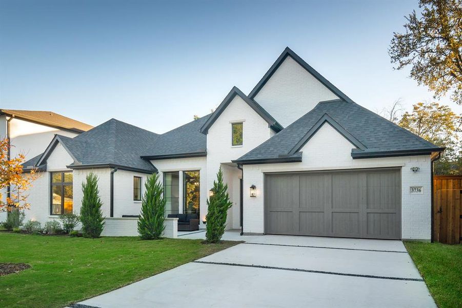 Modern inspired farmhouse featuring concrete driveway, brick siding, a front yard, a shingled roof, and an attached garage Modern inspired farmhouse featuring concrete driveway, brick siding, a front yard, a shingled roof, and an attached garage
