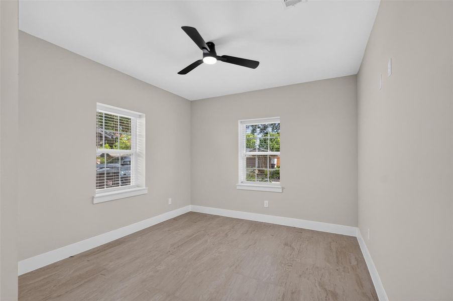 Bright and airy room featuring neutral walls, sleek wood flooring, and a modern ceiling fan, complemented by two windows inviting ample natural light.