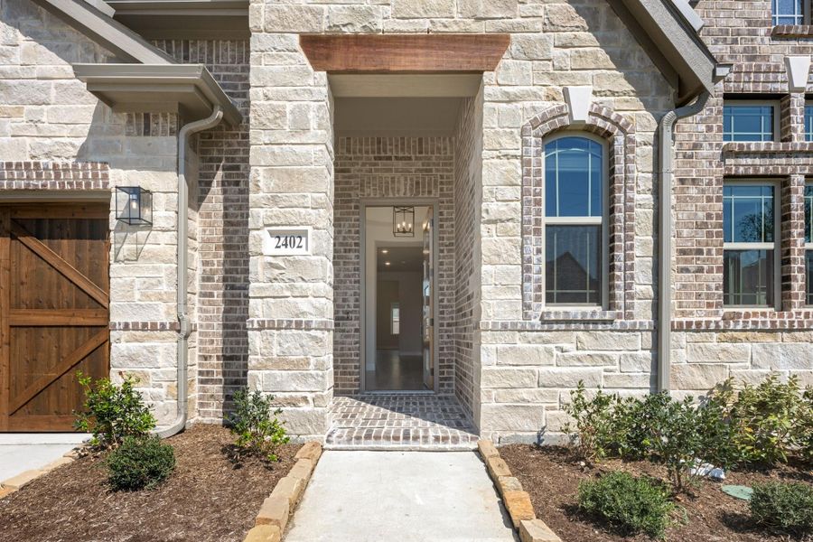 Home entrance with brick and stone exterior, arched doorway, wood garage door, and address number 2402 Home entrance with brick and stone exterior, arched doorway, wood garage door, and address number 2402