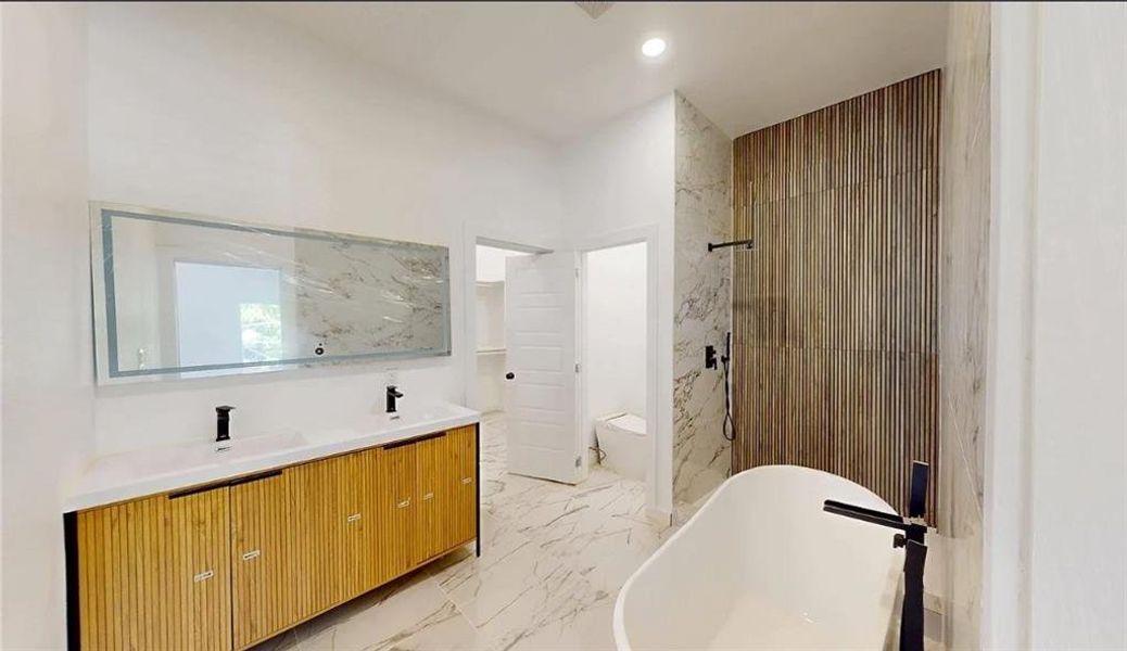 Bathroom featuring a freestanding bathtub with matte black fixtures, a dual vanity with a light wood-finish cabinet and white countertop, and a large illuminated mirror