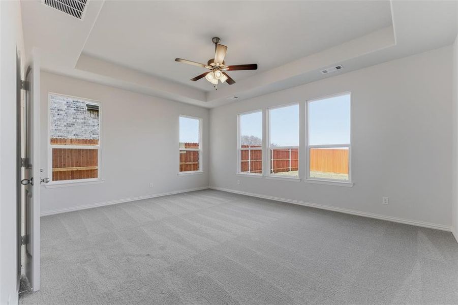 Empty room featuring light carpet, a tray ceiling, and ceiling fan