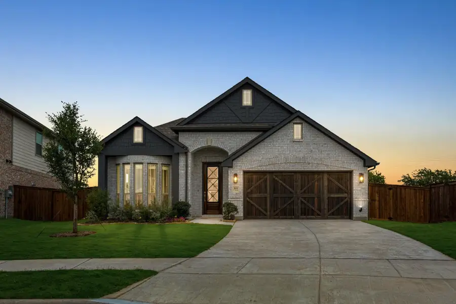 Single-story brick home with dark trim, two-car garage with wood doors, and arched entry at dusk Single-story brick home with dark trim, two-car garage with wood doors, and arched entry at dusk