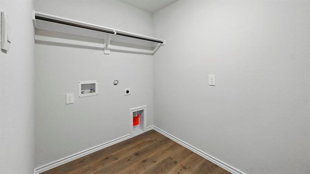 Dedicated laundry space featuring wood-finish flooring, white baseboards, and a built-in wire shelf with hanging rod