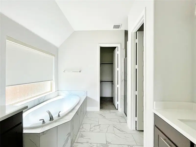 Full bathroom with vanity, a garden tub, light marble finish flooring, a spacious closet, and vaulted ceiling Full bathroom with vanity, a garden tub, light marble finish flooring, a spacious closet, and vaulted ceiling