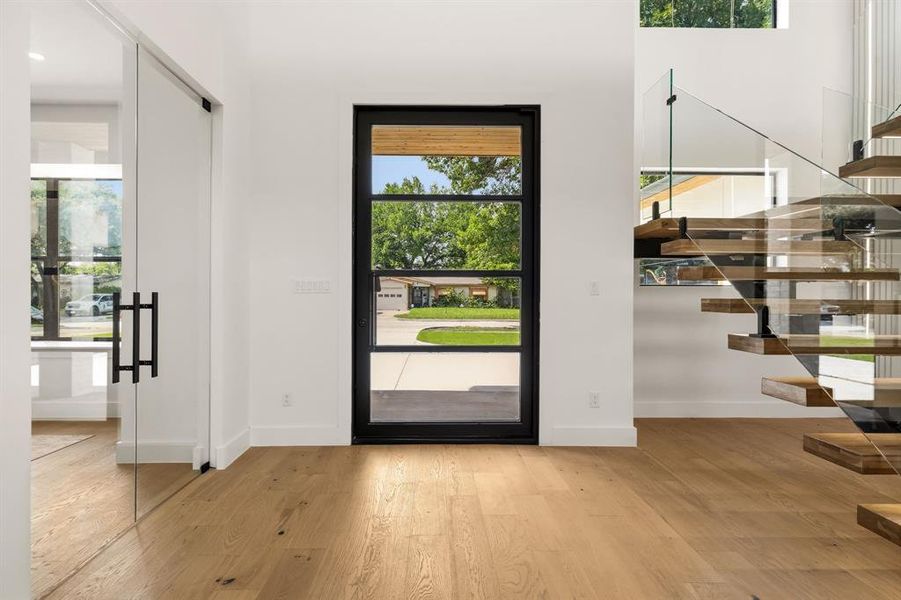 Modern entry featuring a black-framed glass door, wood-finish flooring, and a floating staircase with glass railings