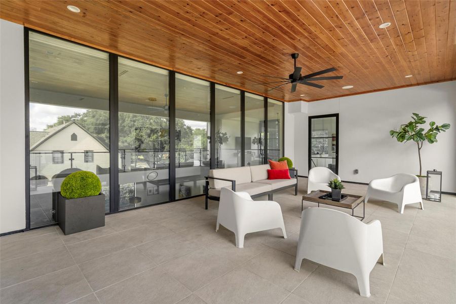 [Upstairs Terrace] The second-floor terrace opens fully to the interior through a wall of glass doors, sheltered by a stained plank ceiling and treetop views.