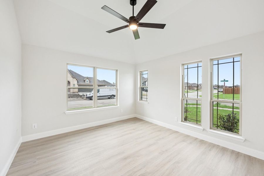 Empty room with light wood floors, ceiling fan, and large windows overlooking a neighborhood street