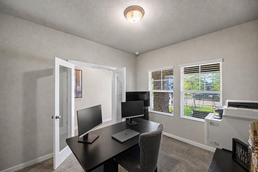 Bright home office with double French doors, ample natural light from two windows, and modern workspace setup.