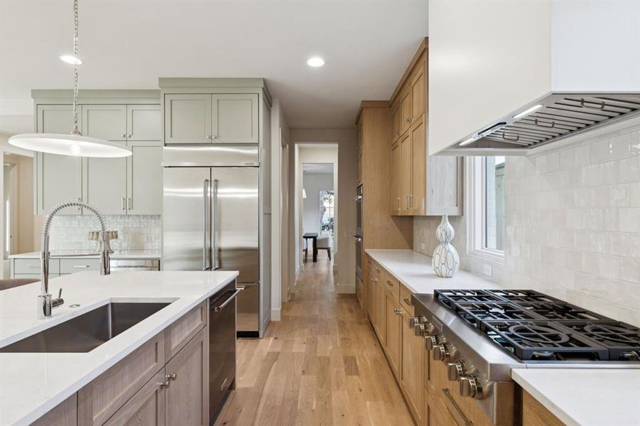 Kitchen with backsplash, stainless steel appliances, light wood-style floors, light countertops, and custom range hood