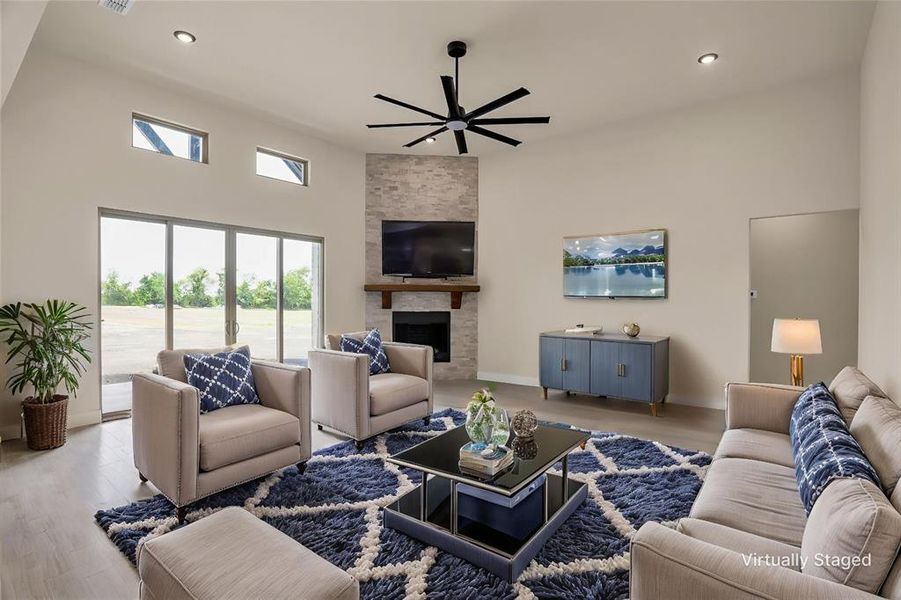 Living area with a ceiling fan, a high ceiling, recessed lighting, a stone fireplace, and wood finished floors Living area with a ceiling fan, a high ceiling, recessed lighting, a stone fireplace, and wood finished floors