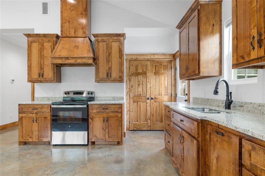 Kitchen featuring electric stove, a sink, custom range hood, concrete flooring, and brown cabinets Kitchen featuring electric stove, a sink, custom range hood, concrete flooring, and brown cabinets