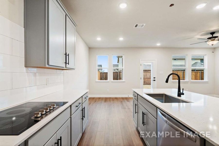 Kitchen with black electric stovetop, sink, stainless steel dishwasher, gray cabinets, and tasteful backsplash