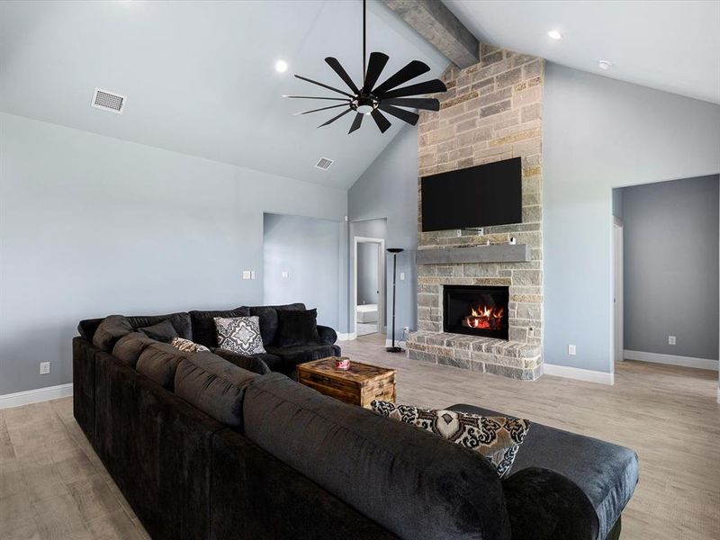 Living room featuring beamed ceiling, light wood-style flooring, high vaulted ceiling, a ceiling fan, and a stone fireplace Living room featuring beamed ceiling, light wood-style flooring, high vaulted ceiling, a ceiling fan, and a stone fireplace