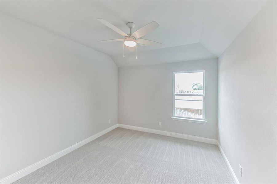 Empty room featuring ceiling fan, lofted ceiling, and carpet flooring