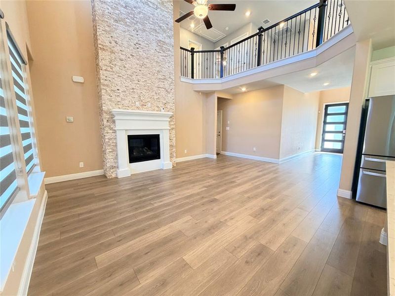 Unfurnished living room with a high ceiling, light wood-style floors, a glass covered fireplace, and a ceiling fan Unfurnished living room with a high ceiling, light wood-style floors, a glass covered fireplace, and a ceiling fan