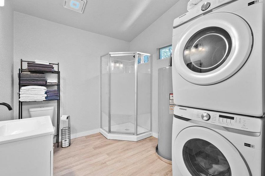 Laundry area featuring light wood finished floors, estacked washer and dryer, electric water heater, and vaulted ceiling.