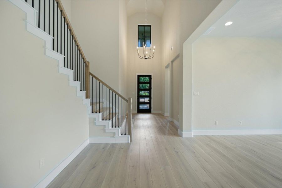 A grand entrance with soaring ceilings, light wood floors, and an elegant staircase.