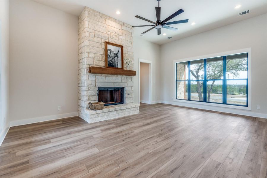 Unfurnished living room with ceiling fan, light wood finished floors, a stone fireplace, and recessed lighting