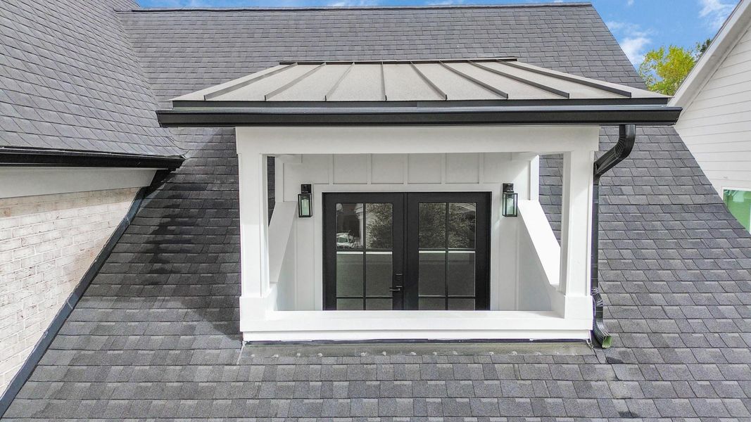 This charming front balcony, with sleek double doors, contemporary lantern lighting, and crisp architectural details, offers an intimate outdoor space ideal for savoring the tranquil, friendly vibes of Timbergrove Manor.