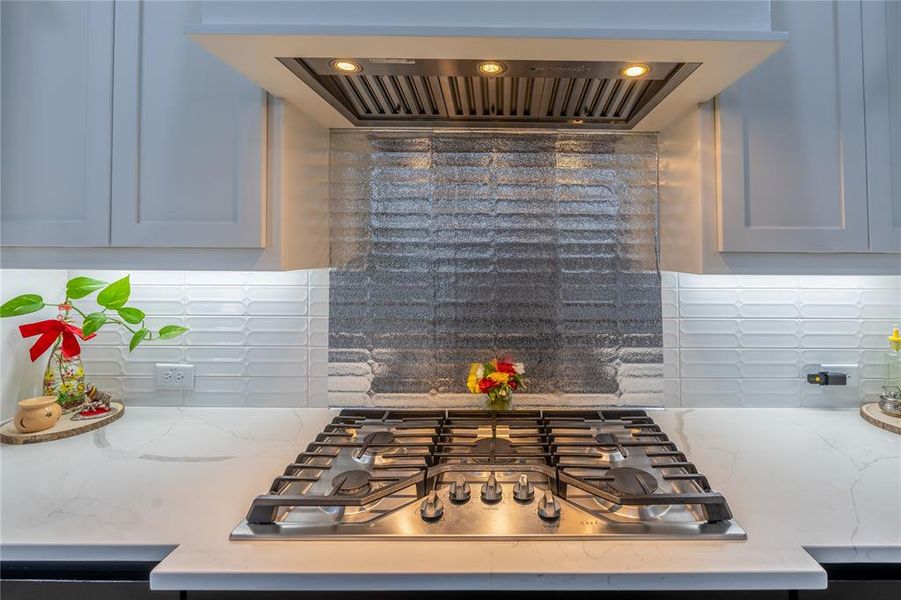 Kitchen featuring range hood, decorative backsplash, light stone counters, and stainless steel gas stovetop