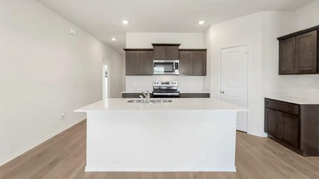 Central kitchen island with white countertop, dark wood-finish cabinetry, stainless steel appliances, and light wood-finish flooring