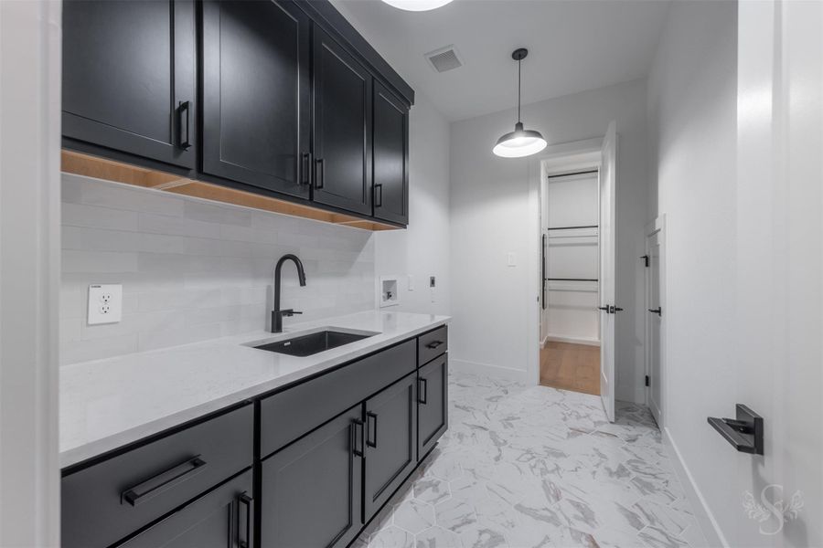 Laundry room with added cabinetry, quartz countertops, and a sink. The laundry room is conveniently connected to the primary bedroom closet. Laundry room with added cabinetry, quartz countertops, and a sink. The laundry room is conveniently connected to the primary bedroom closet.