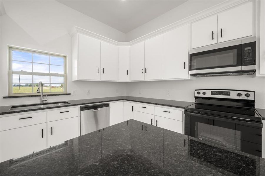 Kitchen featuring appliances with stainless steel finishes, white cabinetry, and dark stone counters Kitchen featuring appliances with stainless steel finishes, white cabinetry, and dark stone counters