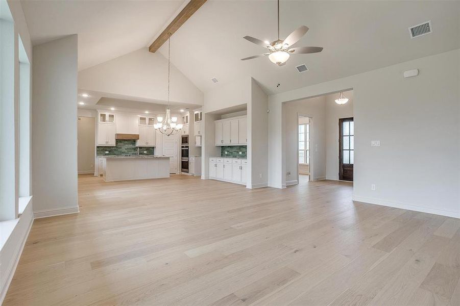 Unfurnished living room featuring high vaulted ceiling, ceiling fan with notable chandelier, light hardwood / wood-style floors, and beam ceiling