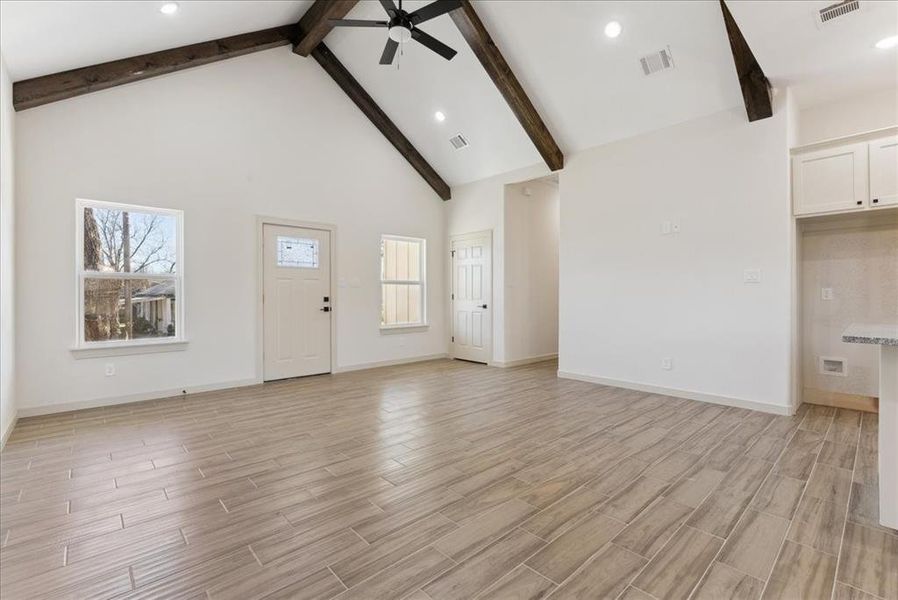 Unfurnished living room with beam ceiling, ceiling fan, high vaulted ceiling, and light wood-type flooring