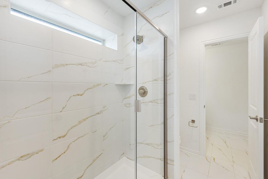 Walk-in shower with marble tile walls, glass door, and small window for natural light Walk-in shower with marble tile walls, glass door, and small window for natural light