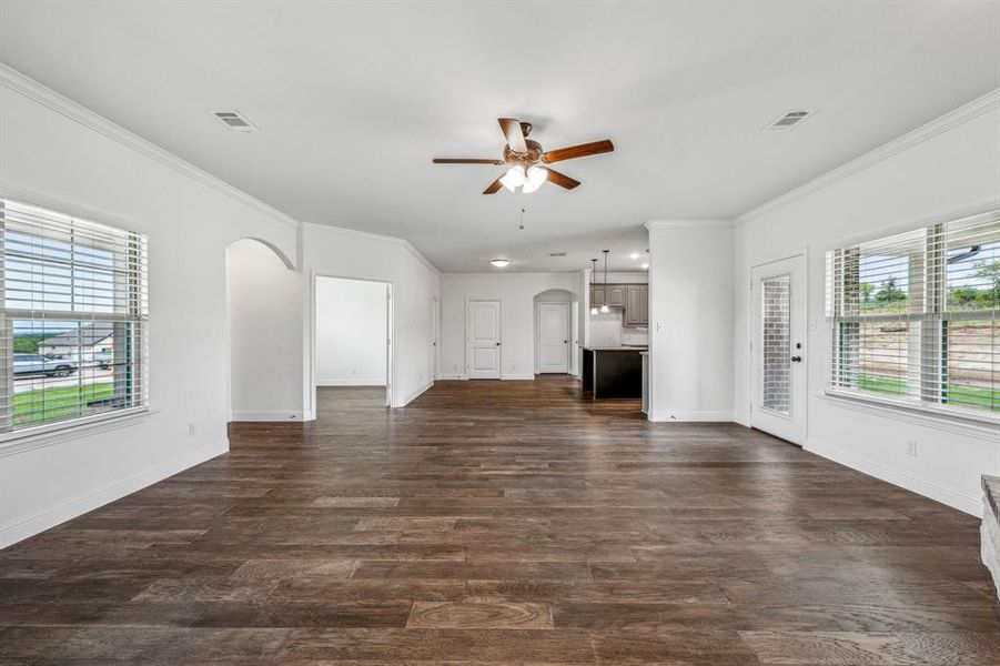 Unfurnished living room with a healthy amount of sunlight, wood-type flooring, crown molding, and ceiling fan