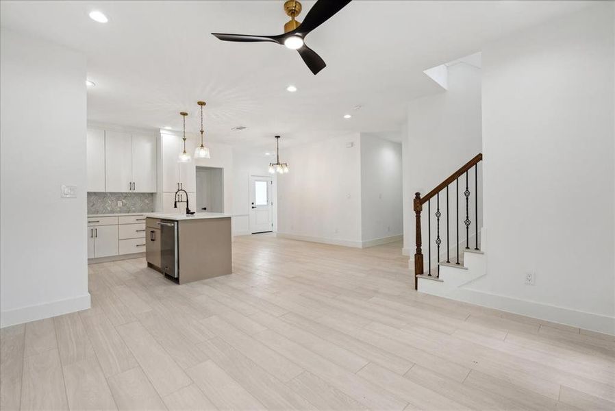 Kitchen featuring an island with sink, ceiling fan with notable chandelier, light hardwood / wood-style floors, decorative light fixtures, and white cabinets