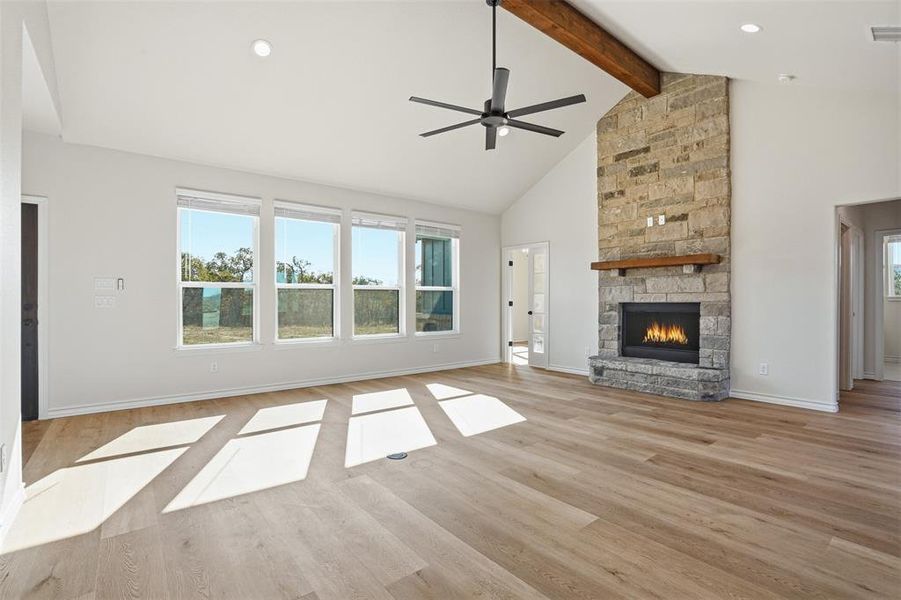 Unfurnished living room with high vaulted ceiling, a fireplace, light wood finished floors, a ceiling fan, and plenty of natural light Unfurnished living room with high vaulted ceiling, a fireplace, light wood finished floors, a ceiling fan, and plenty of natural light