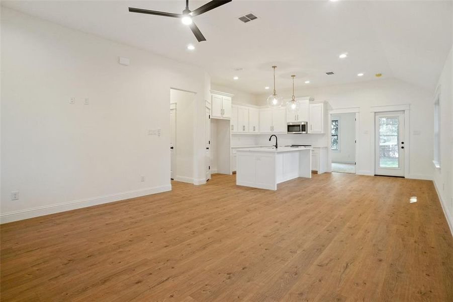 Kitchen with white cabinets, open floor plan, recessed lighting, light wood-style floors, and a center island with sink